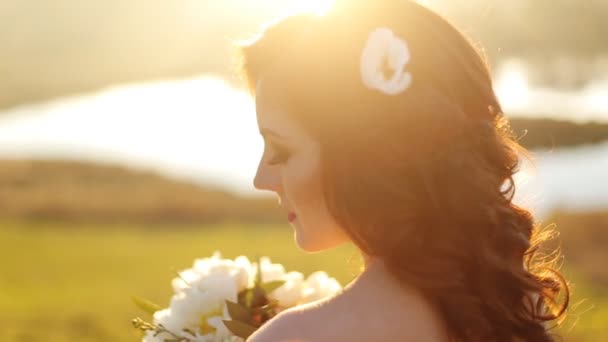 Portrait en gros plan d'une belle jeune mariée brune sexy jeune fille avec des fleurs dans ses cheveux look attrayant dans une robe blanche sur un fond de forêt d'automne et feuilles posant et souriant tourné lentement — Video
