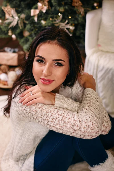 Hermosa mujer sonriente feliz sentada cerca del árbol de Año Nuevo decorado en la sala de estar, con presente en sus manos. Feliz Navidad y Feliz Año Nuevo concepto . — Foto de Stock