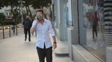 . Güneş gözlüğü takan, şehir merkezinde yürüyen ve telefonla konuşan genç adam. 20'li yıllarda kentsel erkek.