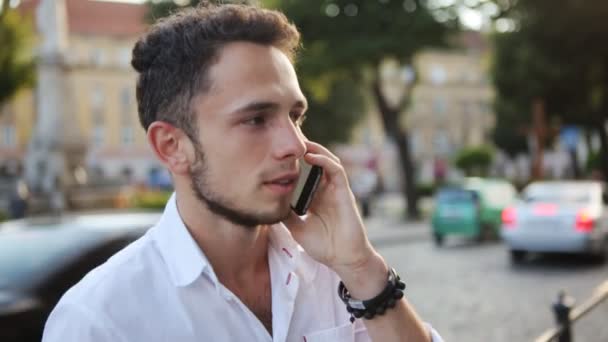 Joven hablando por teléfono móvil en medio de un centro de la ciudad europea. Hombre de unos 20 años . — Vídeo de stock