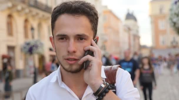 男は、スローモーションで屋外の電話で会話をしています。ヨーロッパの都市の真ん中に携帯電話で話している学生. — ストック動画