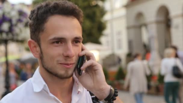 Un hombre sonriente de unos 20 años hablando de un celular al aire libre. Chico guapo hablando por teléfono y haciendo una hermosa sonrisa . — Vídeos de Stock