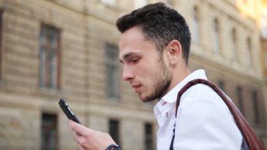 Telefonun ekranında izliyor ve gülümseyen çekici adam. Açık havada smarphone kullanarak kendi 20s olumlu erkek