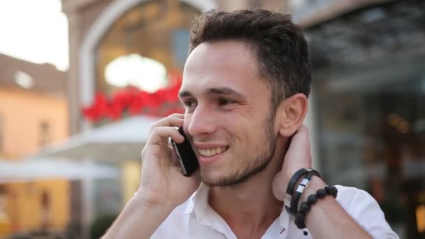 Joven macho sosteniendo el teléfono, sonriendo y tocando su cuello . — Vídeos de Stock