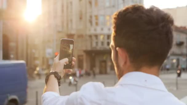 Hombre de 20 años tomando una foto panorámica en la calle al atardecer . — Vídeo de stock