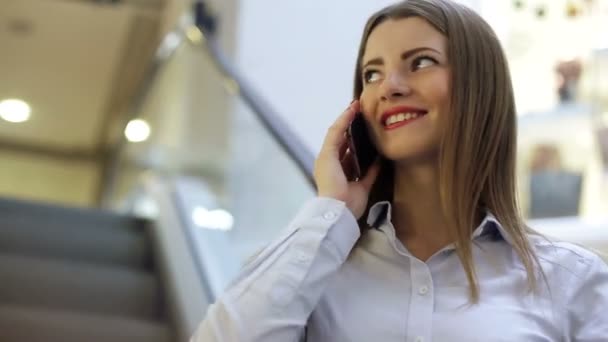 Jovem sorrindo mulher está falando em seu telefone celular em um shopping — Vídeo de Stock