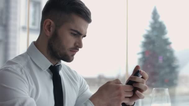 Feliz joven navegando por Internet en el teléfono inteligente sentado en la cafetería — Vídeos de Stock