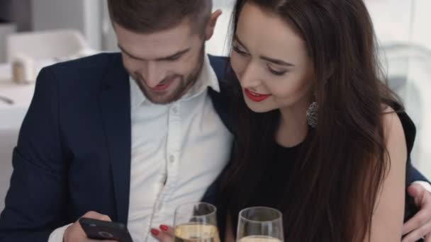 Linda pareja sentada en el restaurante mirando el teléfono inteligente en un día soleado — Vídeos de Stock
