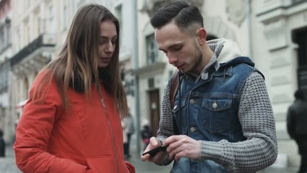 Pareja joven usando dispositivo móvil al aire libre en el centro de la ciudad europea . — Vídeos de Stock