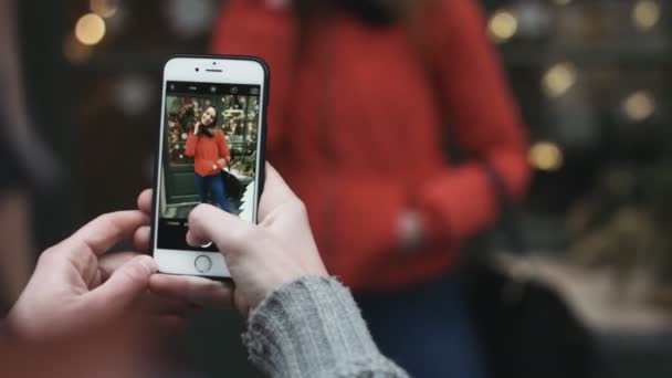 Close-up de um homem tirando fotos de sua menina atraente ao ar livre. Cara usando seu dispositivo móvel para tirar fotos de seu amigo . — Vídeo de Stock