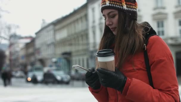 Mujer joven está esperando a sus amigos al aire libre y utilizando el teléfono inteligente para enviar mensajes de texto. Chica está recibiendo un mensaje en su dispositivo móvil . — Vídeo de stock