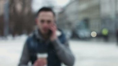 Genç çekici erkek bir paket servisi olan restoran elinde kahve ile kameraya doğru hareket. Telefonla konuşurken ve güzel gülümseme yapıyor adam.