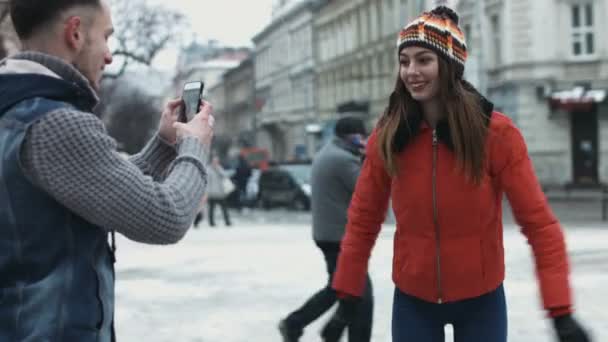 Guy fotí krásné dívky venku pomocí svého mobilního zařízení. Atraktivní žena dělat dojem na kameru. — Stock video