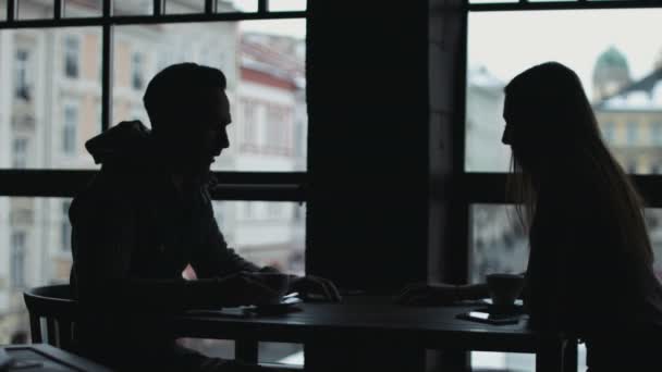 Obraz sylwetka słodki para siedząc w kawiarni naprzeciwko ogromne okna, rozmowy i trzymając się za ręce siebie. — Wideo stockowe