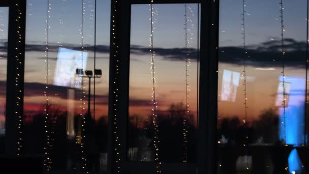 Bild av djupa röda solnedgången bakom fönstret stora inredda av jul ljus. Molnen ovan går snabbt. — Stockvideo
