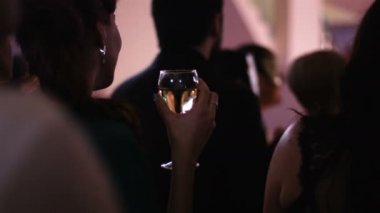 Genç çekici kadın ayakta geri kamera ve bir bardak beyaz şarap partide tutmak ve bir performans nereye gidiyor aşamada izlerken.