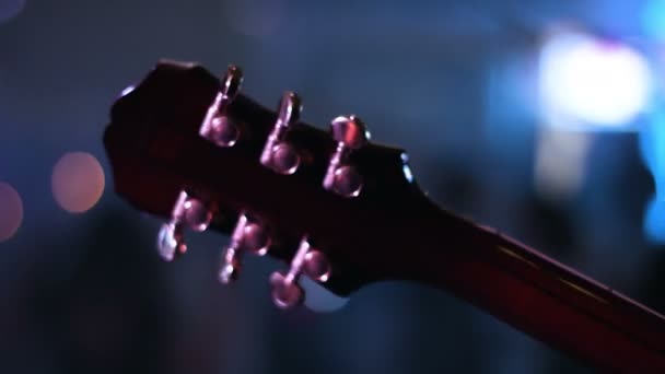 Detalj bilder av gitarr headstock som spelas av musiker på en konsert. Folk dansar på en suddig bakgrund. — Stockvideo