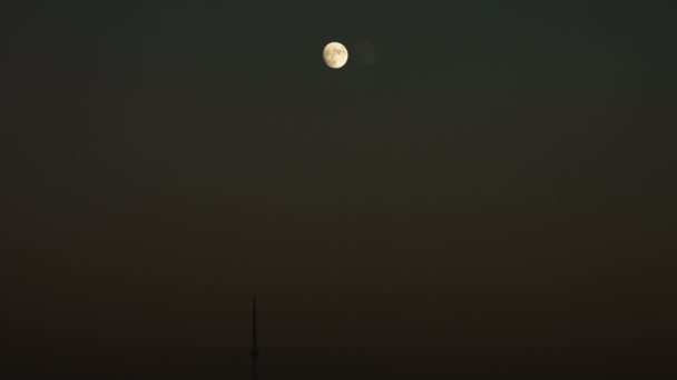 Incomplete moon at night sky with a steel spire of a building on a footage. — Stock Video