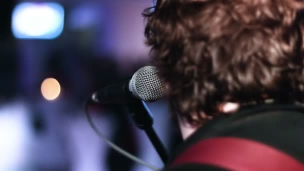 Närbild bild av sångare som sitter mot en mikrofon vid scenen. Skäggig man sitter tillbaka till kameran innan showen startar. — Stockvideo