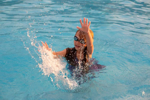Dívka v plaveckých brýlích se baví a cáká v bazénu. — Stock fotografie