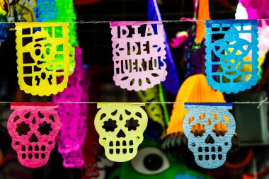 Üzerinde Dia De Muertos yazıları olan canlı bir kağıt kafatası gösterisi. Meksika Ölüler Günü geleneği, adaklar, yemek, renkler, dekorasyonlar ve papel picado, La Catrina.