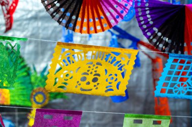 Kablodan sarkan parlak bir kağıt fener gösterisi, belirgin bir sarı kafatası feneri ile birlikte. Meksika Ölüler Günü geleneği, adaklar, yemek, renkler, dekorasyonlar ve papel picado, La Catrina.