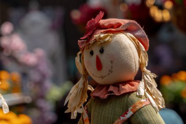 Yeşil elbiseli ve turuncu şapkalı bir korkuluk bir demet çiçeğin önünde duruyor. Meksika Ölüler Günü geleneği, adaklar, yemek, renkler, dekorasyonlar ve papel picado, La Catrina.