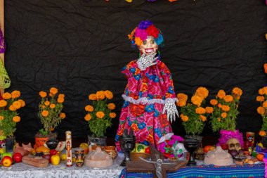 Bir Catrina çeşitli meyve ve sebzelerle bir masanın önünde duruyor. Meksika Ölüler Günü geleneği, adaklar, yemek, renkler, dekorasyonlar ve papel picado, La Catrina.