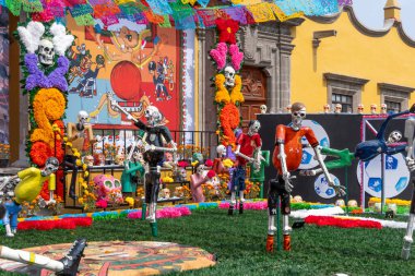 Bir grup iskelet sahada futbol oynuyor. İskeletler renkli kostümler giymişler. Meksika Ölüler Günü geleneği, adaklar, yemek, renkler, dekorasyonlar ve papel picado, La Catrina.