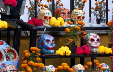 Süslü kafatasları ve çiçeklerle dolu bir masa. Masa çiçekler ve kafataslarıyla dolu. Meksika Ölüler Günü geleneği, adaklar, yemek, renkler, dekorasyonlar ve papel picado, La Catrina.