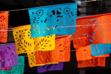 Çiçekler ve yıldızlar da dahil olmak üzere çeşitli tasarımları olan renkli kağıt fenerler sallanıyor. Meksika Ölüler Günü geleneği, adaklar, yemek, renkler, dekorasyonlar ve papel picado, La Catrina.