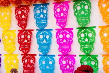 Duvarda renkli kağıt kafatasları asılı duruyor. Kafatasları farklı renk ve boyutlarda. Meksika Ölüler Günü geleneği, adaklar, yemek, renkler, dekorasyonlar ve papel picado, La Catrina.