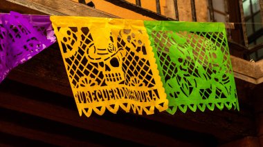 Üzerinde kafatası olan yeşil ve mor bir kağıt fener. Kafatası yeşil kağıdın üzerinde. Meksika Ölüler Günü geleneği, adaklar, yemek, renkler, dekorasyonlar ve papel picado, La Catrina.