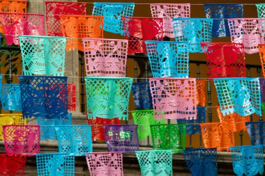 Renkli bir kağıt fener gösterisi balkondan sarkıyor. Fenerler çeşitli renklerdedir. Meksika Ölüler Günü geleneği, adaklar, yemek, renkler, dekorasyonlar ve papel picado, La Catrina.