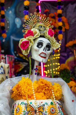 Bir iskelet, kafasının üstünde kafatası olan çiçekli bir kostüm giyer. Meksika Ölüler Günü geleneği, adaklar, yemek, renkler, dekorasyonlar ve papel picado, La Catrina.