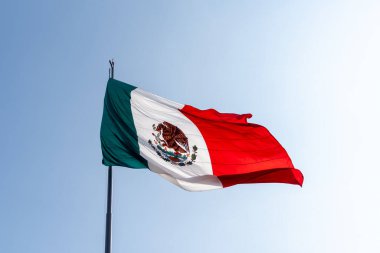 Kırmızı, beyaz ve yeşil bir bayrak. Arkasında mavi bir gökyüzü var..