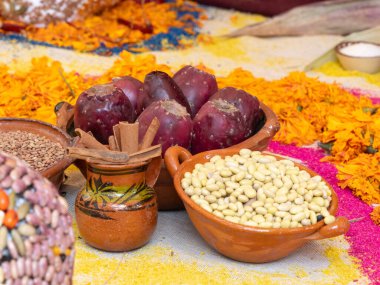 Renkli ve davetkar bir atmosferi olan bir masa. Masanın üzerinde. Fasulyeler daha büyük bir kasede. Meksika Ölüler Günü geleneği, adaklar, yemek, renkler, dekorasyonlar ve papel picado, La Catrina.