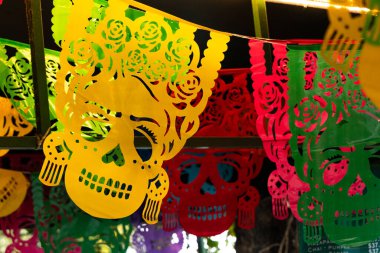 Renkli bir kağıt kafatası ve çiçek gösterisi. Kafatasları farklı renk ve boyutlarda. Meksika Ölüler Günü geleneği, adaklar, yemek, renkler, dekorasyonlar ve papel picado, La Catrina.