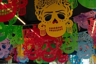 Tavandan sarkan renkli kağıt kafatasları. Kafatasları farklı renk ve boyutlarda. Meksika Ölüler Günü geleneği, adaklar, yemek, renkler, dekorasyonlar ve papel picado, La Catrina.