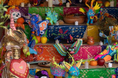 Çeşitli biblolar ve meyveler de dahil olmak üzere renkli bir Meksika sanat ve süslemesi. Meksika Ölüler Günü geleneği, adaklar, yemek, renkler, dekorasyonlar ve papel picado, La Catrina.