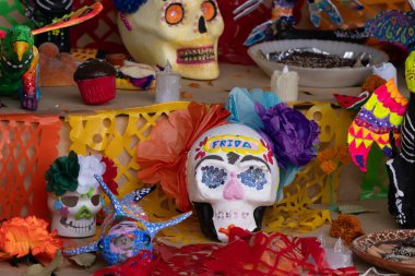 Üzerinde kafatası ve diğer süslemeler olan bir masa. Kafatası çiçeklerle süslenmiş. Meksika Ölüler Günü geleneği, adaklar, yemek, renkler, dekorasyonlar ve papel picado, La Catrina.