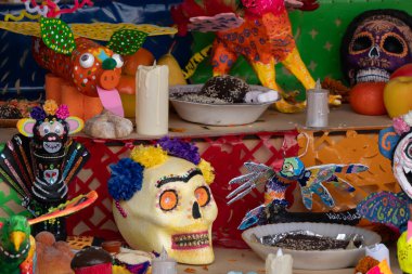 Kafatası, mum ve kase gibi bir sürü renkli süslemeleri olan bir masa. Meksika Ölüler Günü geleneği, adaklar, yemek, renkler, dekorasyonlar ve papel picado, La Catrina.