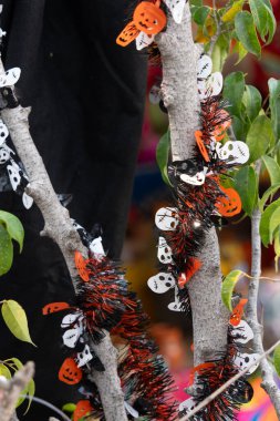 Bir ağaç dalı, kafatasları ve balkabakları da dahil olmak üzere Cadılar Bayramı süslemeleriyle süslenir. Meksika Ölüler Günü geleneği, adaklar, yemek, renkler, dekorasyonlar ve papel picado, La Catrina.