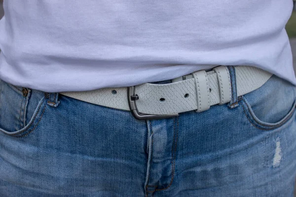 Beyaz tişörtlü, kot pantolonlu ve beyaz kemerli bir kız.