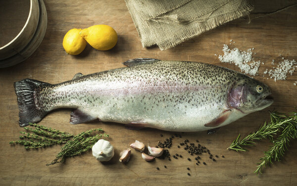 Large Trout on Wooden Background surrounded by Herbs and Spices
