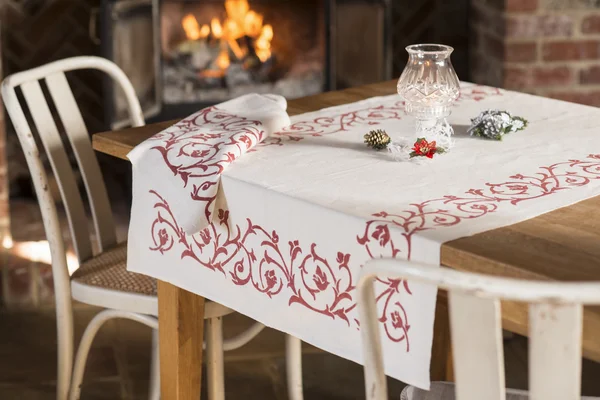 Bílý ubrus s květinovým vzorem červená na stole poblíž krbu — Stock fotografie