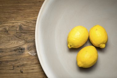 Bir ahşap yüzeyde bir sığ taş kase üç limon