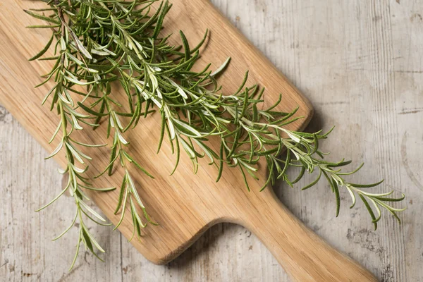 Rosemary deitado em uma tábua de corte de madeira em uma madeira mais velha e usada — Fotografia de Stock