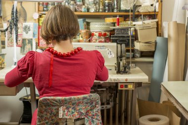 Oturmuş ve dikiş makinesi üzerinde çalışan kadın terzi