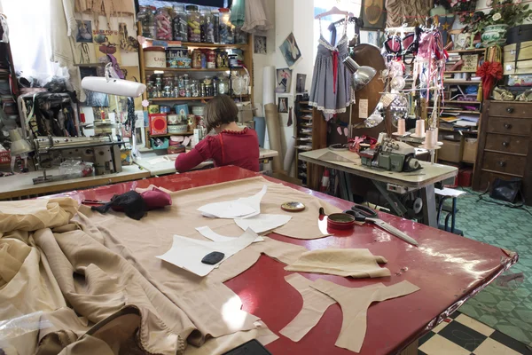 Tailor's Cutting Table with Seamstress and Shop in the Backgroun — Stock Photo, Image